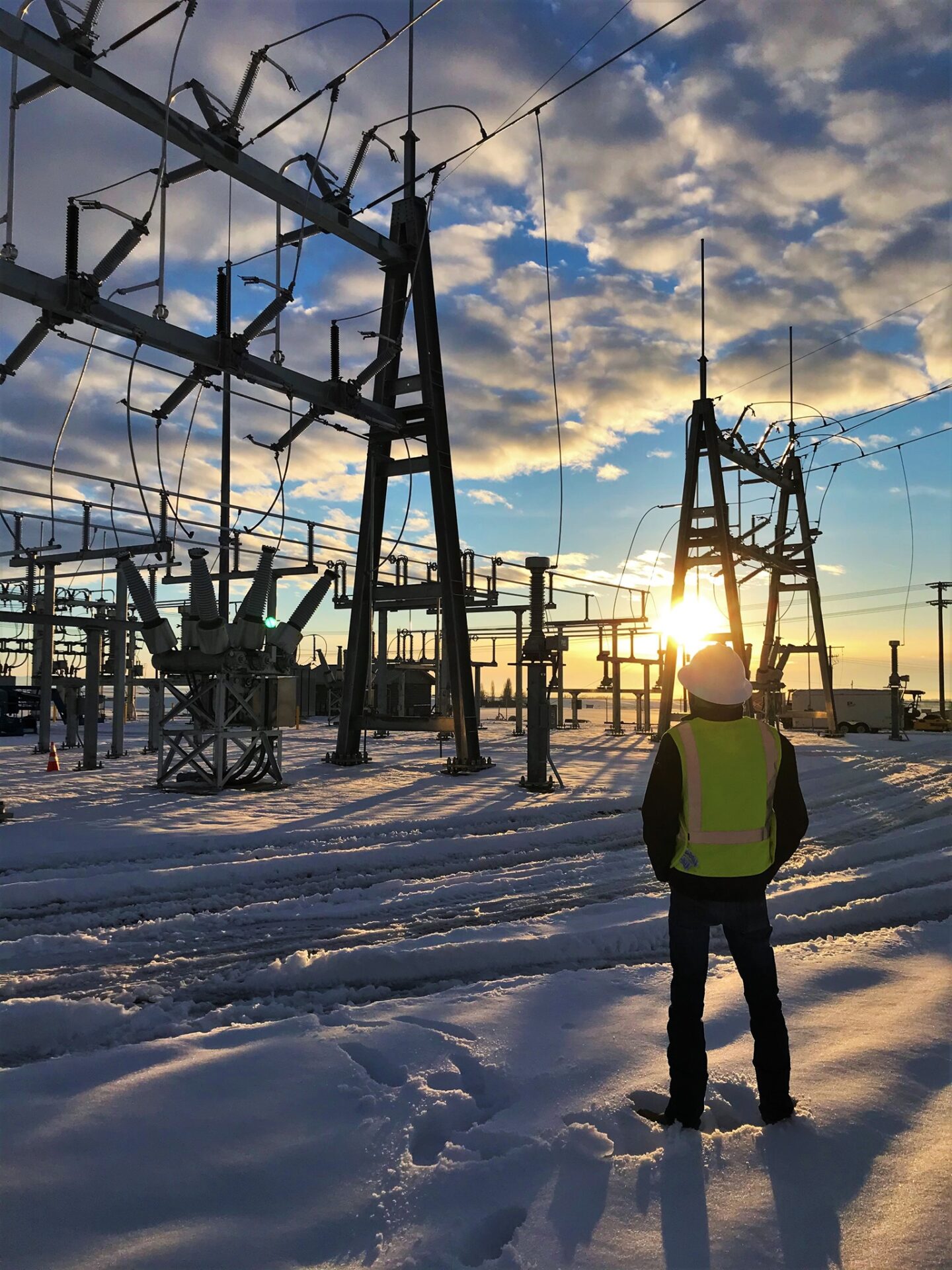 worker standing in snow looking at power lines